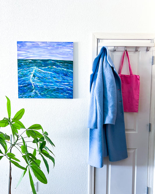 Entryway with a painting of West Beach on the wall, a plant and a coat ant tote hanging 
